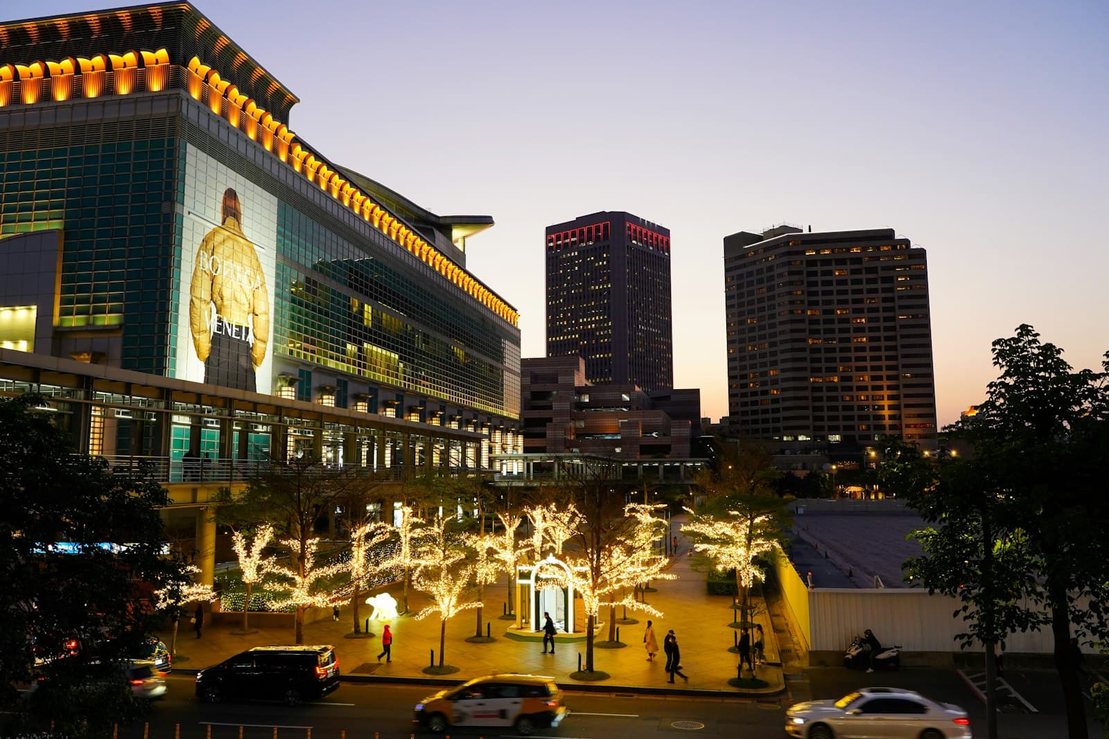 An illuminated retail plaza and hotel towers at dusk